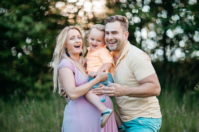 Happy pregnant woman with family standing on field at park