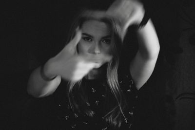 Portrait of woman making finger frame against black background