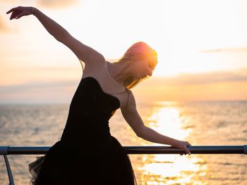 Woman standing by sea against sky during sunset