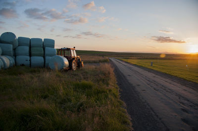 Road amidst field against sky during sunset