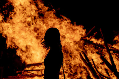 Silhouette woman standing by bonfire on field at night