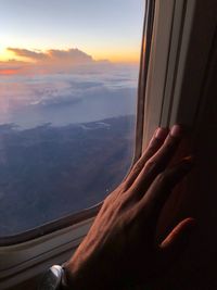Cropped image of hand against sky seen through airplane window
