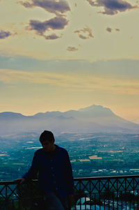 Man looking at cityscape against sky during sunset