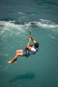 A man flies on a rope across the river.