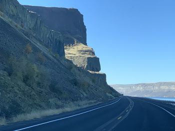 Road leading towards mountains against clear sky