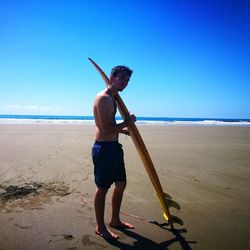 Full length of man standing on beach against clear blue sky