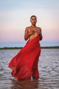 Portrait of young woman standing in sea against sky