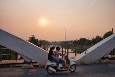 People on motorcycle against sky during sunset