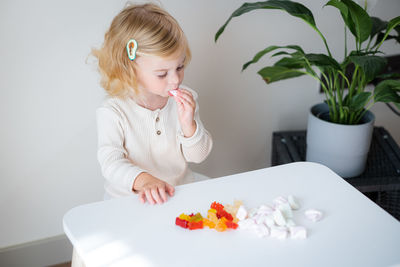 Adorable cute caucasian blonde curly-haired baby girl two, three year old eating jelly, sweet gummy