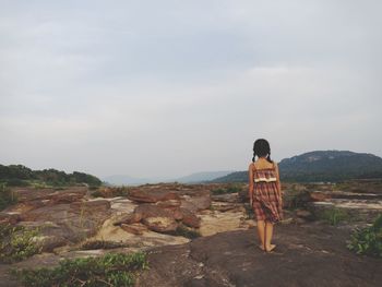 Rear view of woman standing on rock against sky