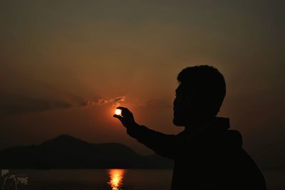 Optical illusion of silhouette man holding sun above sea at sunset