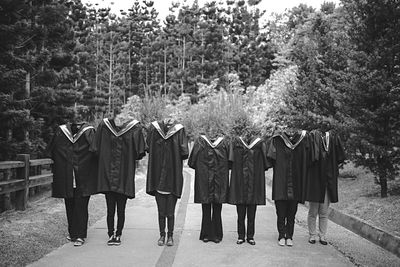 Friends wearing graduation gown standing on footpath against trees