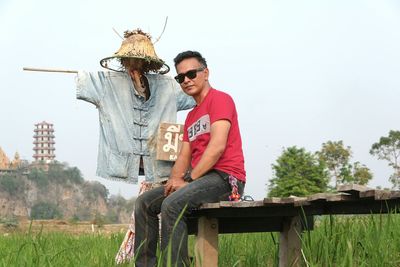 Man sitting by scarecrow on field