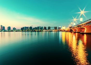 Illuminated buildings by river against sky at night