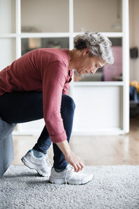 Side view of mature woman tying shoelace at home