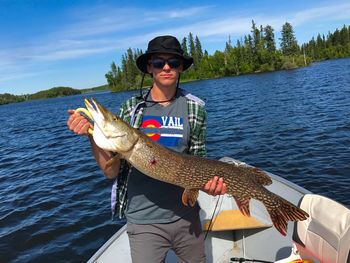 Portrait of smiling young man holding fish while standing in boat against river