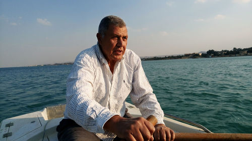 Young man sitting in sea against sky