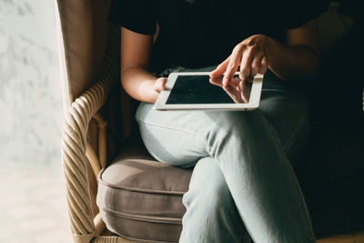 Midsection of woman sitting with legs crossed at knee using digital tablet at home