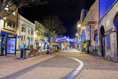 Illuminated street amidst buildings in city at night