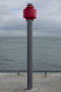 Red wooden post in sea against sky