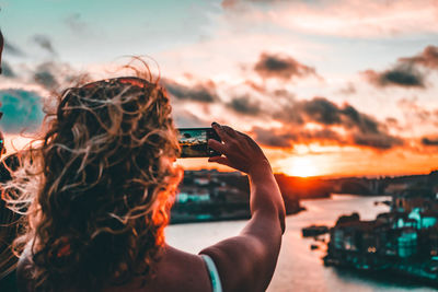 Midsection of woman photographing sea against sky during sunset