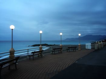 Street lights by sea against sky at dusk