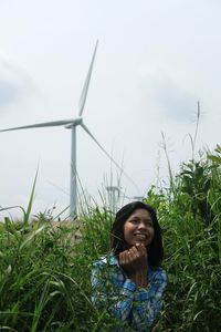Smiling woman standing amidst plants against windmill and sky
