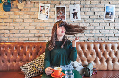 Beautiful young woman drinking against wall