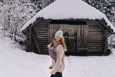Full length of woman standing in front of  snow covered house