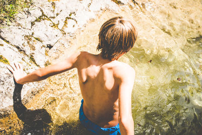 Rear view of shirtless boy standing in lake
