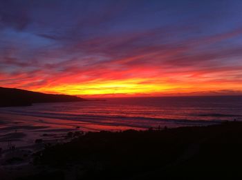 Scenic view of beach against dramatic sky during sunset