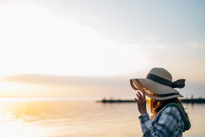 Rear view of woman standing at beach against sky during sunset