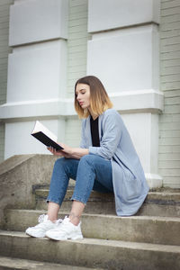 Young woman reading book while sitting outdoors