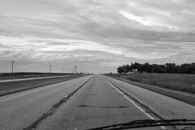 Empty road amidst field against sky