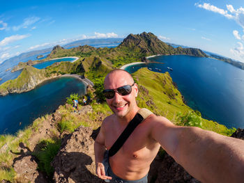Fish-eye lens portrait of shirtless man standing on cliff by sea