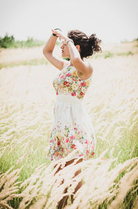 Side view of young woman in dress standing on field against clear sky during sunny day