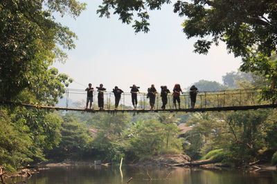 Friends standing on rope bridge over lake in forest