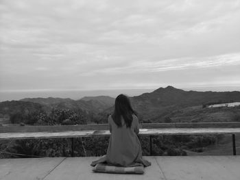 Rear view of woman sitting against mountains