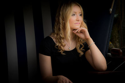Young woman looking away while sitting against black background