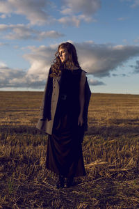 Woman in grey coat and black dress in field at sunset in autumn