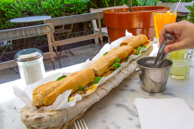 Cropped image of person holding serving tongs by sandwich on table