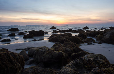 Rocks on beach against sky during sunset