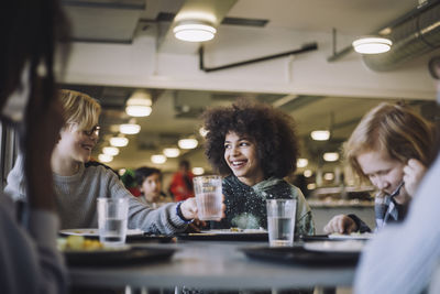 Boy passing drinking glass to friend during lunch break at school