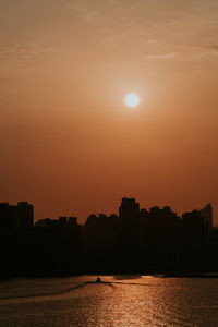 Silhouette buildings by sea against orange sky