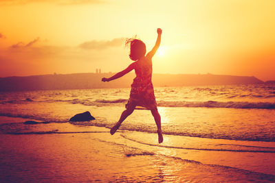 Young woman jumping on beach during sunset