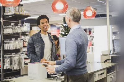 Smiling male customer with kettle box talking to mature owner while standing in electronics store