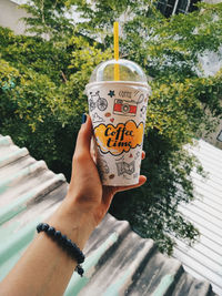 Close-up of hand holding ice cream cone against trees