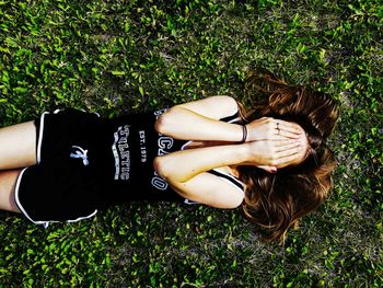 Directly above shot of woman covering face while lying on grassy field