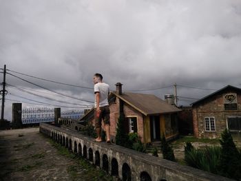 Man on bridge by buildings against sky