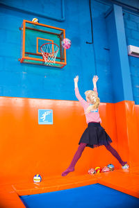 Full length of woman jumping against orange wall